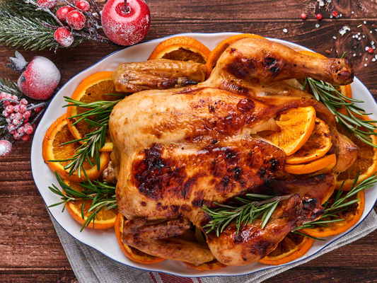 KI generiert: Ein Brathähnchen mit Orangen und Rosmarin auf einem Teller, umgeben von Weihnachtsdekoration.