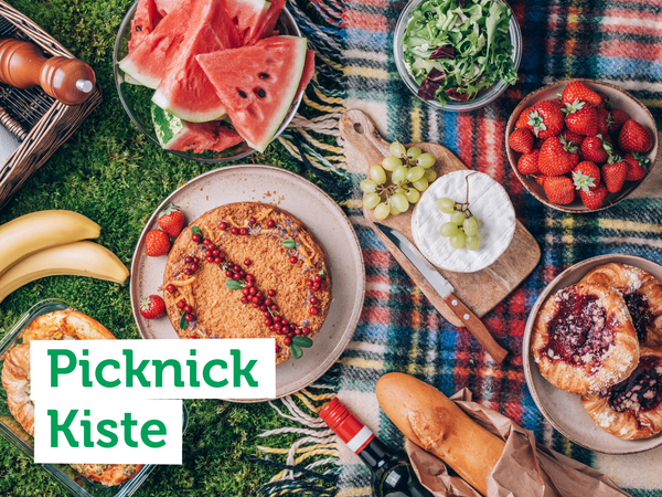 KI generiert: Ein Picknick auf einer Decke mit Obst, Käse und Gebäck. Text: "Picknick Kiste".