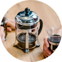 KI generiert: Eine French Press und eine Hand mit einem Glas Kaffee auf einem Holztisch.