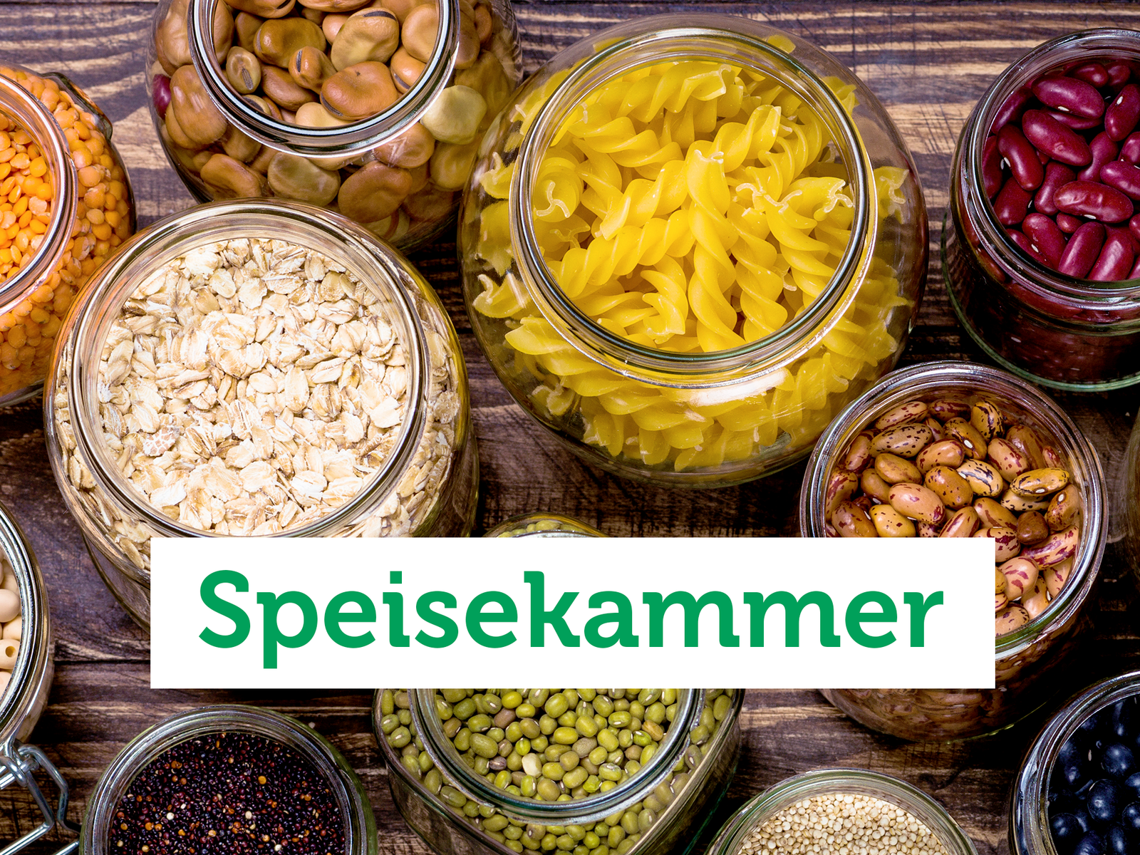 Vogelperspektive auf eine Holzfläche auf der verschieden große Vorratsgläser gefüllt mit Hülsenfrüchten, Nudeln und Haferflocken angeordnet sind.
