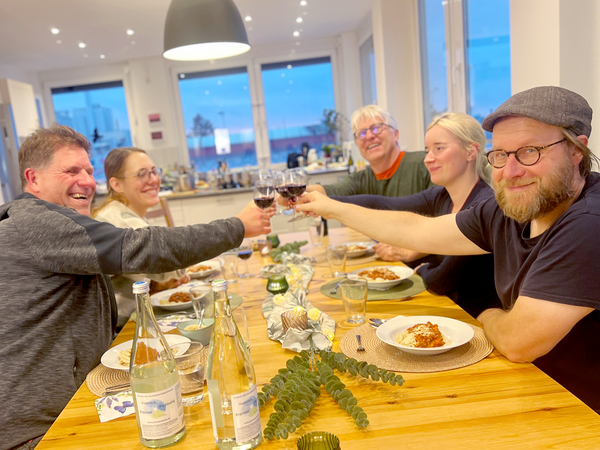 KI generiert: Sechs Personen stoßen mit Weingläsern an einem Tisch mit gedecktem Abendessen an.