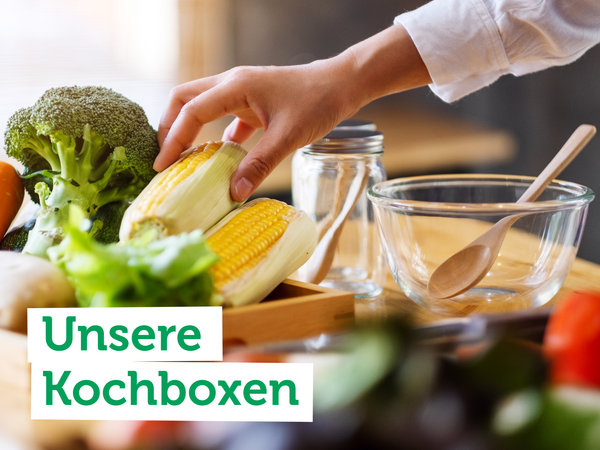 Eine Hand greift nach Mais und Brokkoli in der Küche. Text: "Unsere Kochboxen".