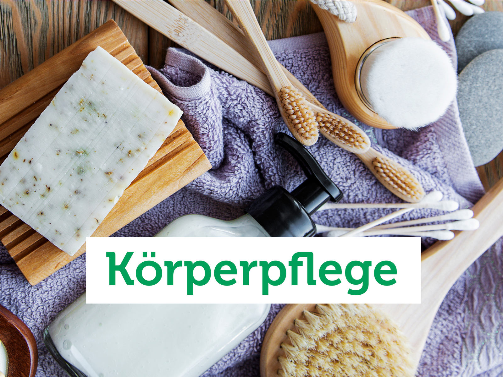 Vogelperspektive auf eine Holzfläche auf der Körperpflegeprodukte wie Seife am Stück und in der Flasche, Handtuch und Bürsten liegen.