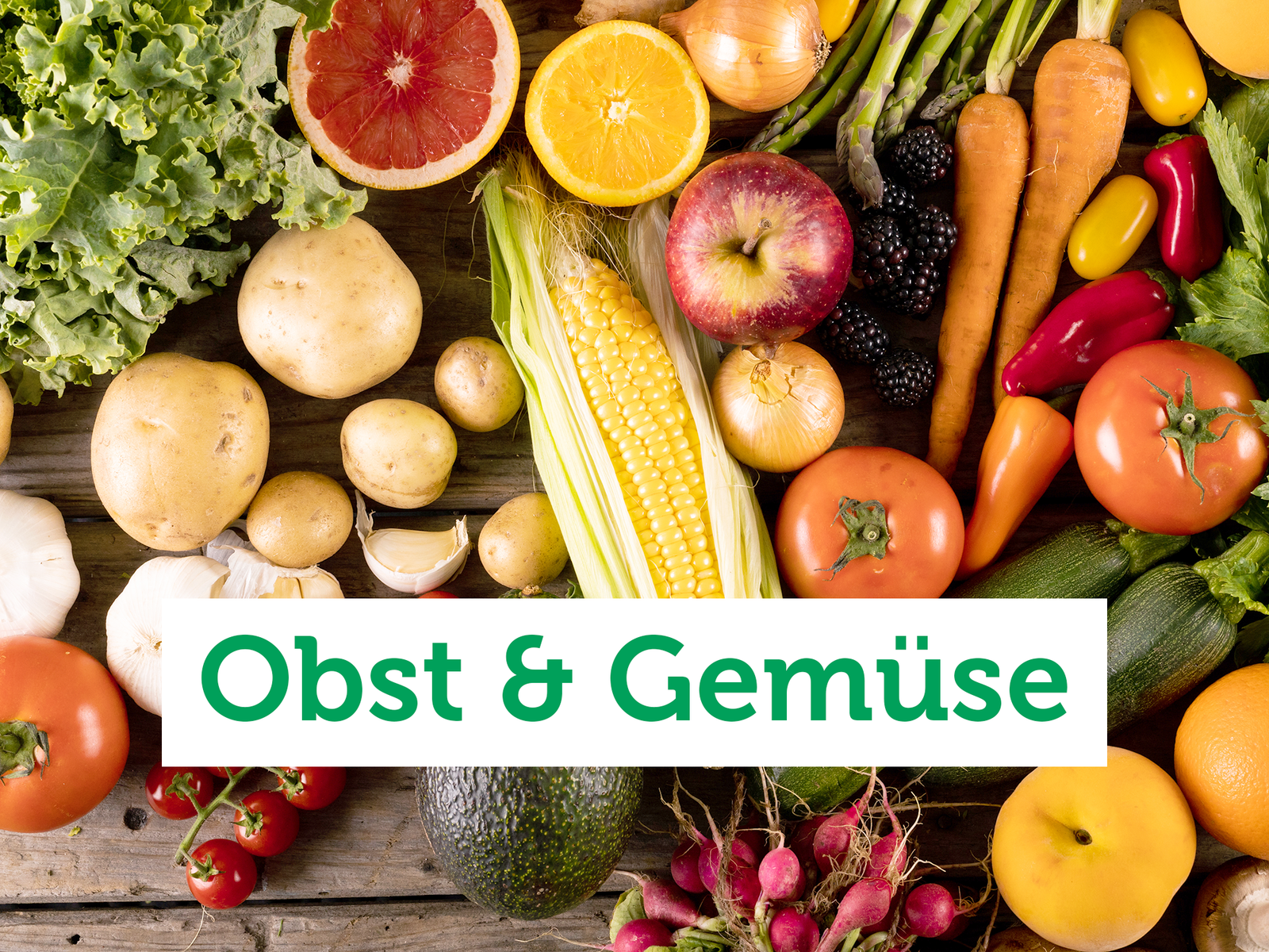 Vogelperspektive auf eine Holzfläche auf der bunt gemischtes Obst und Gemüse liegt, wie Mais, Zucchini, Möhren, Orangen und Radieschen