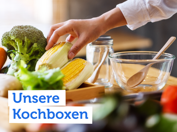 KI generiert: Eine Hand greift Maiskolben, daneben Gemüse. Text: "Unsere Kochboxen".