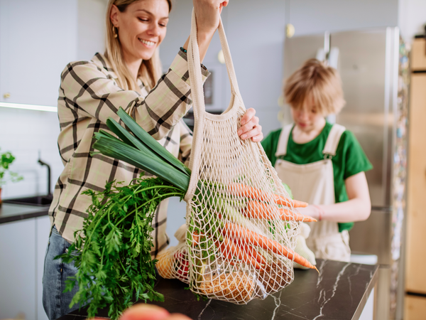 KI generiert: Personen räumen frisches Gemüse aus einem Netzbeutel in der Küche aus.