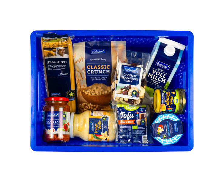 Vogelperspektive auf eine blaue Plastikkiste voller verpackter Lebensmittel wie Milch, Nudeln, Aufstrich und Müsli