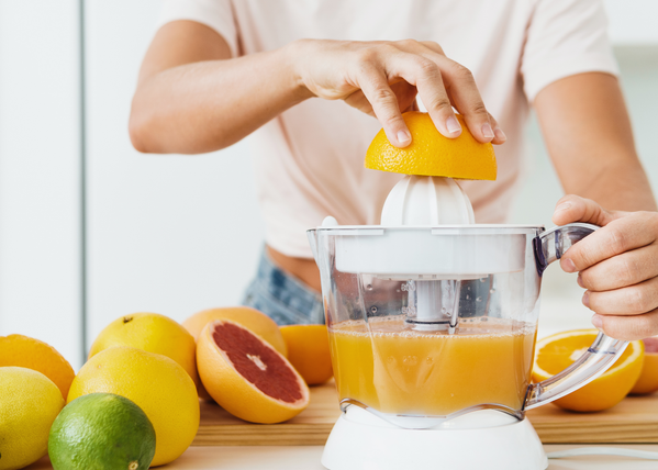 Eine Person presst eine Orange mit einer elektrischen Saftpresse aus.