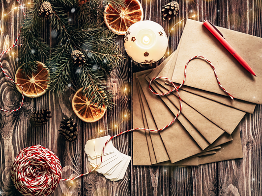 KI generiert: Weihnachtliche Bastelszene mit Umschlägen, Stift, Kerze, Tannenzweigen und getrockneten Orangenscheiben.