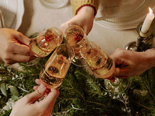 KI generiert: Vier Personen stoßen mit Sektgläsern an, feierliche Stimmung mit Kerze und Tannenzweigen.