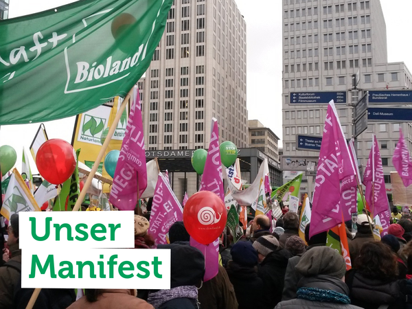 Protest mit bunten Fahnen und Ballons. Text: "Unser Manifest".