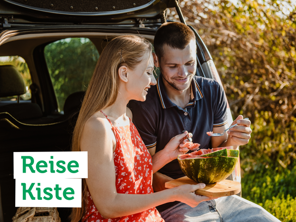 KI generiert: Ein Paar isst Wassermelone im Freien. Text: "Reise Kiste".