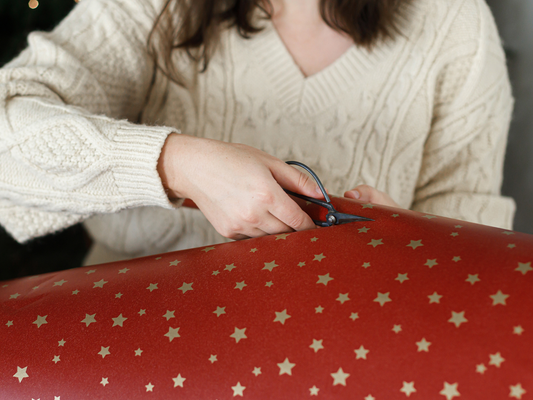 KI generiert: Person schneidet rotes Geschenkpapier mit Sternenmotiven.