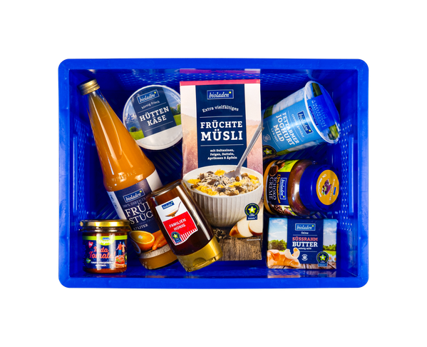 KI generiert: Eine blaue Kiste voller BIO-Lebensmittel von "bioladen*". Hauptinhalt: Früchtetee, Müsli, Joghurt, Hüttenkäse.
