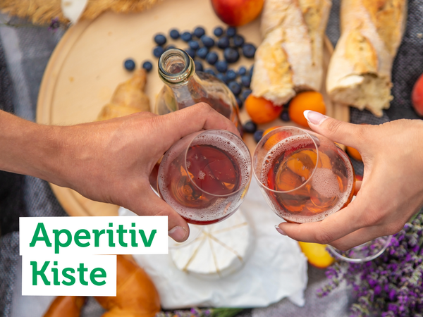 KI generiert: Zwei Personen stoßen mit Gläsern an, umgeben von Brot, Käse und Früchten. Text: "Aperitiv Kiste".