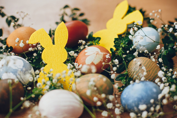 KI generiert: Bunte Ostereier und gelbe Hasensilhouetten, umgeben von Blumen und Blättern.