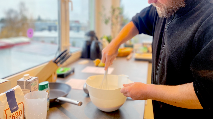 KI generiert: Eine Person rührt Zutaten in einer Schüssel in einer Küche. Im Vordergrund stehen weitere Backzutaten.