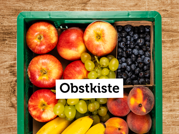 Eine gefüllte Obstkiste mit Äpfeln, Trauben, Bananen, Blaubeeren und Pfirsichen. Text: "Obstkiste".