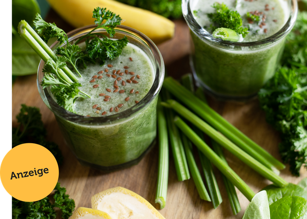 Zwei grüne Smoothies mit Petersilie, Sellerie und Leinsamen auf einem Tisch. Text: "Anzeige".