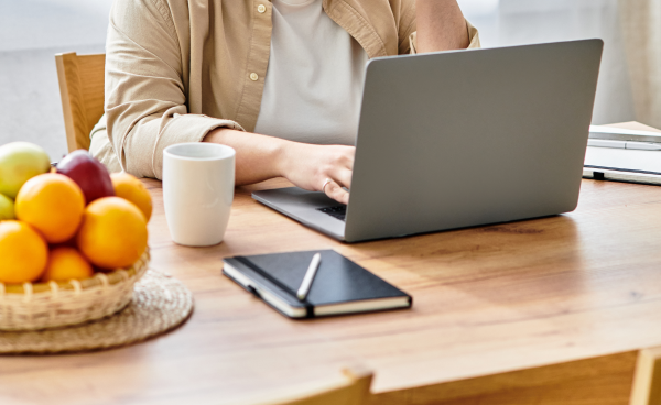 KI generiert: Person arbeitet am Laptop, Obstschale und Notizbuch auf dem Tisch.