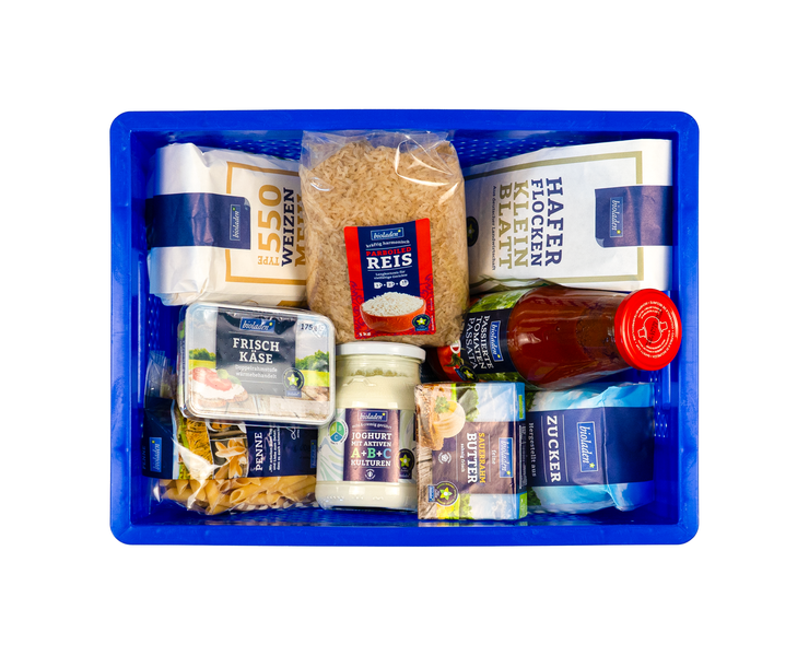Vogelperspektive auf eine blaue Plastikkiste voller verpackter Lebensmittle wie Mehl, Reis, Tomatensoße, Butter und Frischkäse
