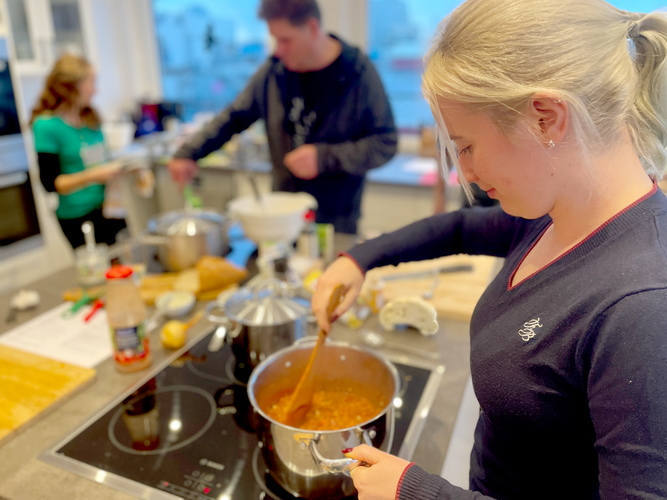 KI generiert: Menschen kochen zusammen in einer Küche, mit einer Person, die in einem Topf rührt.
